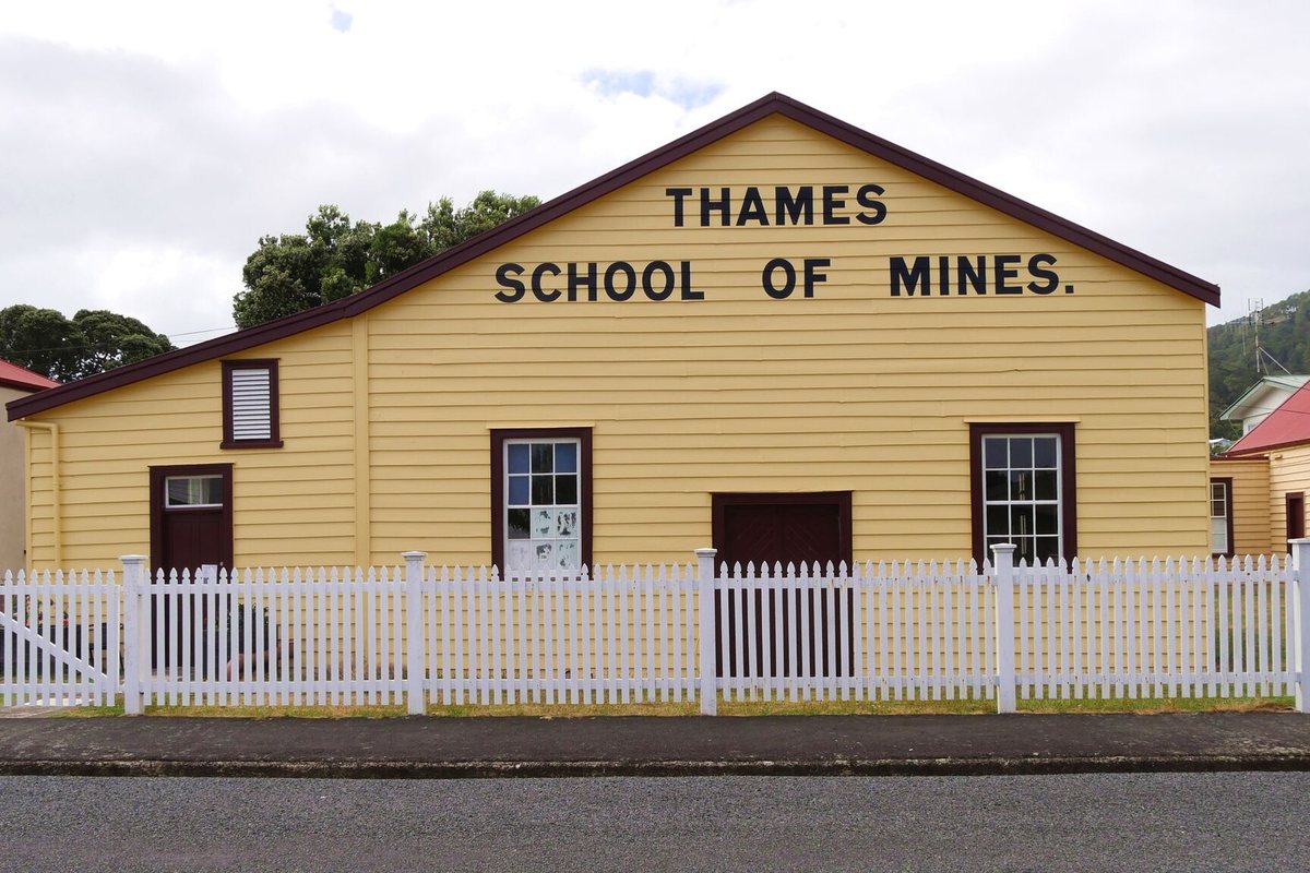 The yellow weatherboard Thames School of Mines building behind a white picket fence